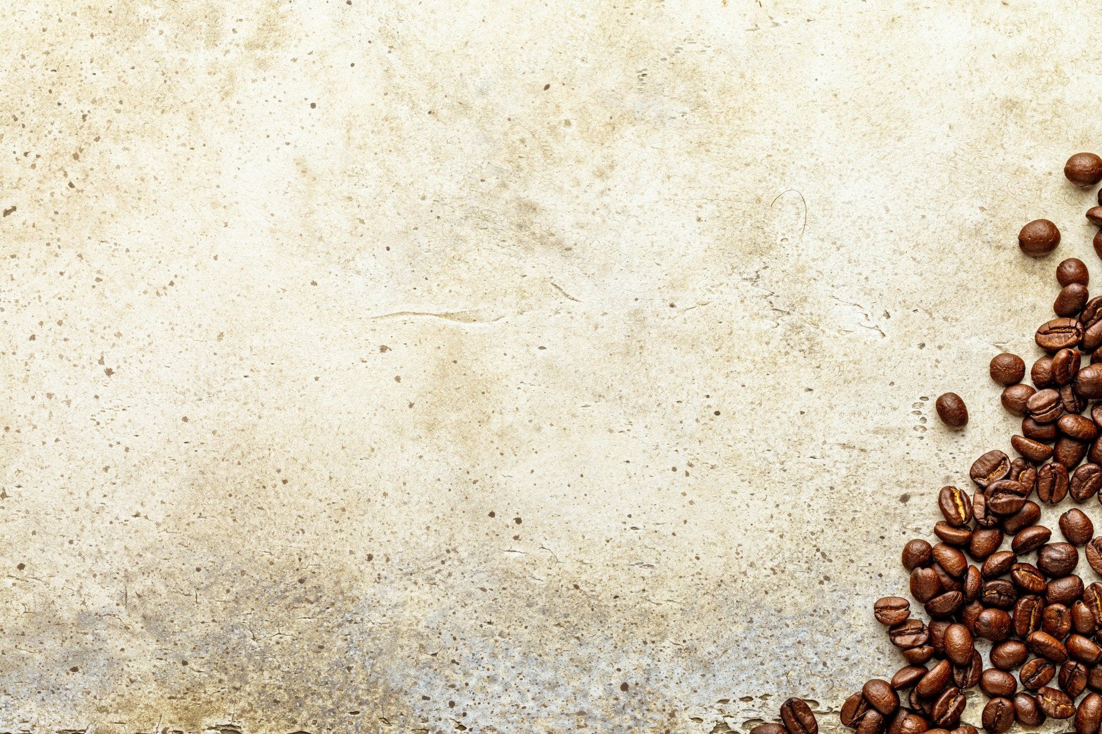Roasted coffee beans gathered at the edge of a pale surface.